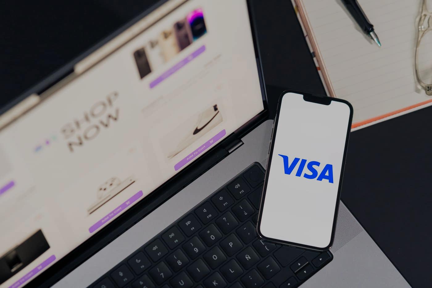 An online shop open on a laptop, with a phone propped against it showing the Visa mark.